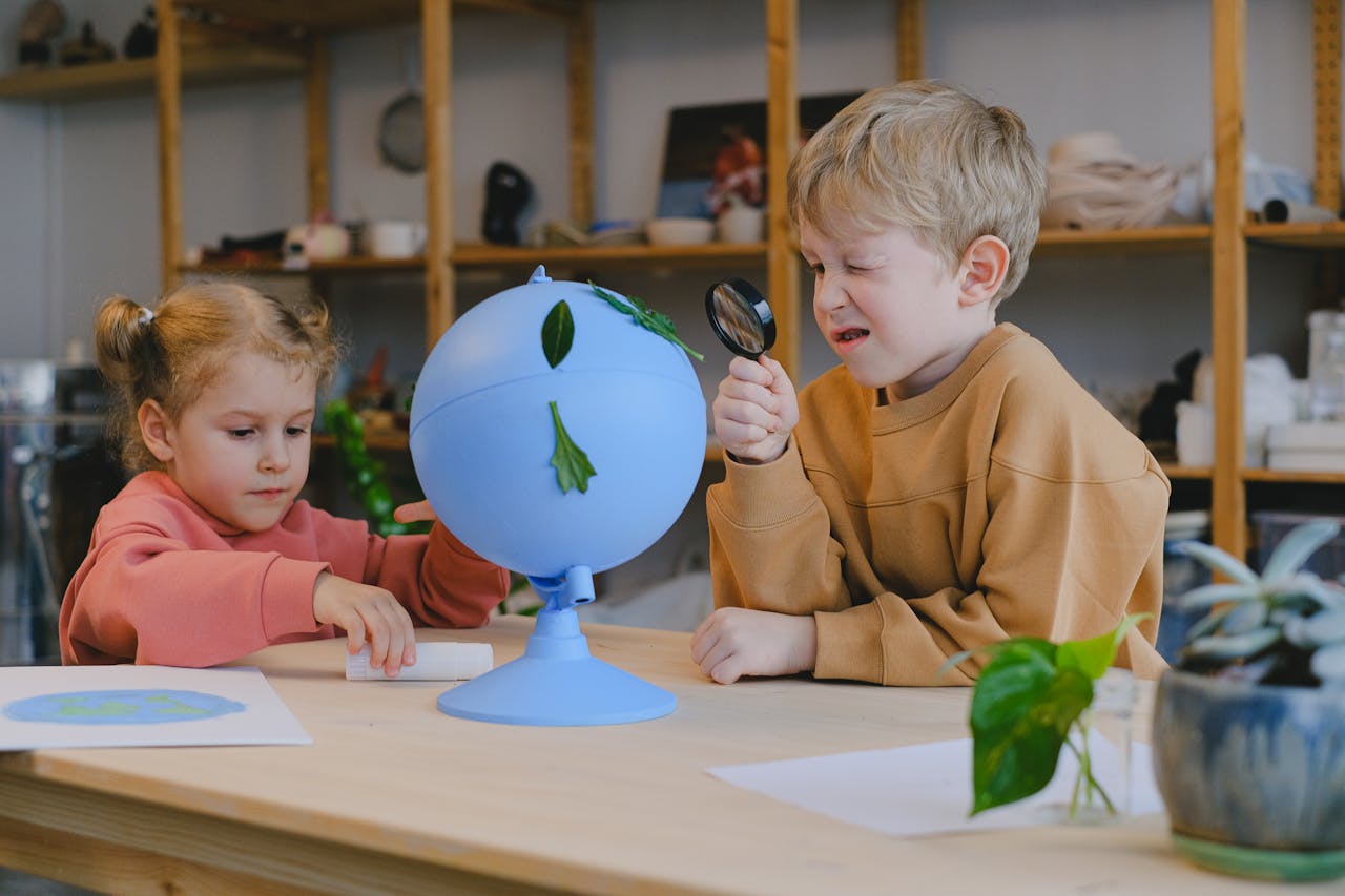 Two children using a magnifying glass to explore a globe with leaves, fostering curiosity and environmental awareness.