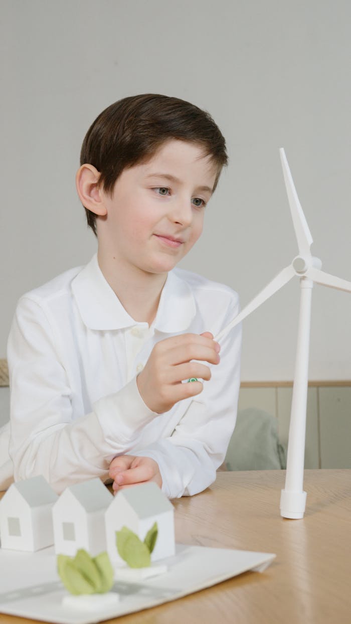 A young boy interacts with a miniature wind turbine model indoors, fostering interest in renewable energy.