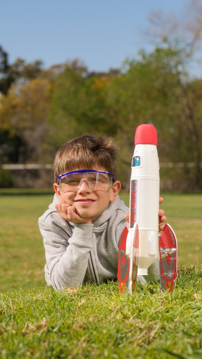 A cheerful boy lying on grass, playing with a toy rocket outdoors on a sunny day.