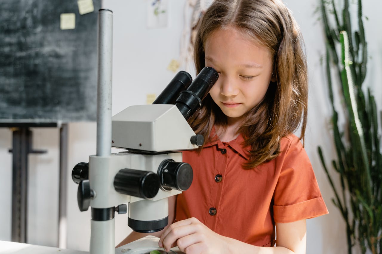 A curious girl examining a sample using a microscope in a classroom setting, focused on learning science.