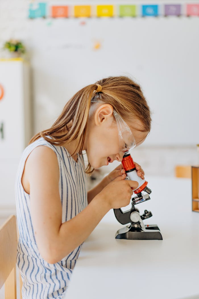 A young girl exploring science education using a microscope indoors, showcasing curiosity and learning.